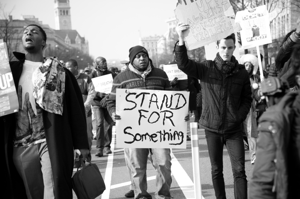 Photo of protesters, a white man is prominate.  a drak skinned man at the center of the phone holds a sign reading "   Photo from Shutterstock.jpg